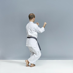 Fototapeta na wymiar Sportsman in white karategi and with a black belt performs formal karate exercises on a gray background