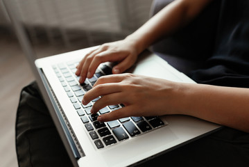 Studying concept. Close-up view of female student in casual clothes typing on laptop`s keyboard, sitting on home.
