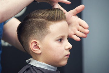 Barber shop. Barber makes hairstyle to a boy with styling gel. - 225572482