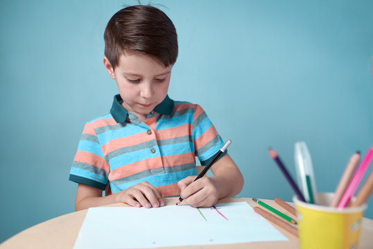 Caucasian boy carefully drawing with colorful pencils at home.