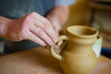 Professional male potter working in workshop, studio - putting handle on ceramic jar. Handmade, small business, crafting work concept