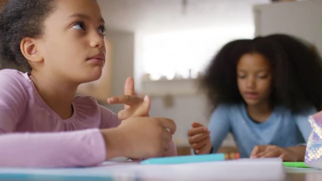 Two young girls work on their homework in their kitchen at home