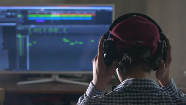 sound producer in headphones relaxing with raised arms in the studio, back view