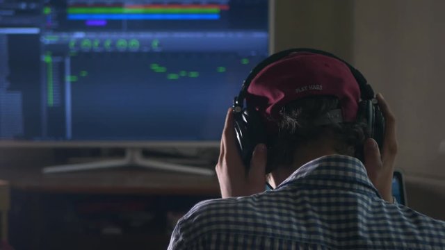 back view of sound engineer in snapback and holding headphones on head monitoring music in studio