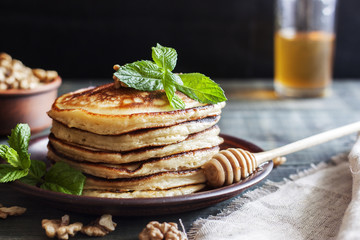 On the table there is a dish with pancakes, honey and nuts.