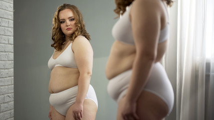 Fat lady attentively looking at her mirror reflection, accepting oversize body