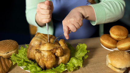 Lady carving roughly roast chicken with fork and knife, unhealthy nutrition