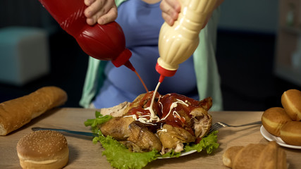 Obese girl pouring unhealthy ketchup and mayonnaise on fatty roast chicken