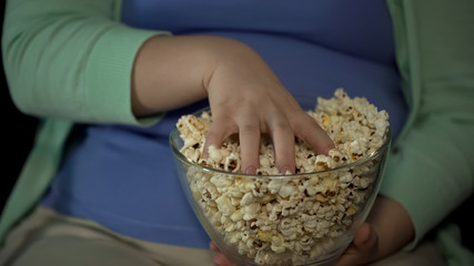 Chubby woman taking handful of fatty popcorn, sedentary lifestyle, overweight
