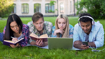 Mixed-race students lying on grass and preparing for exams, university education