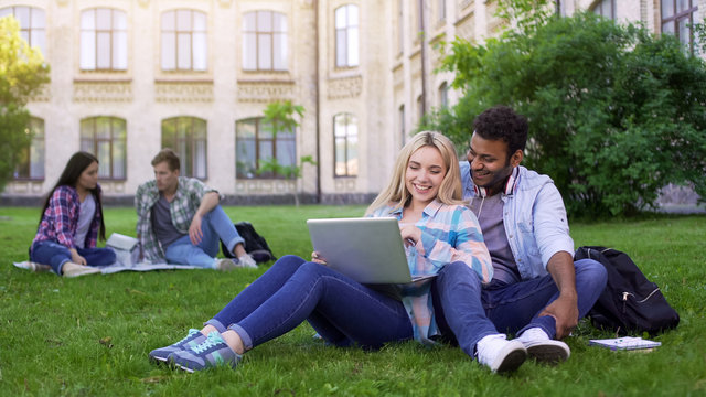 Students sitting on grass and watching funny video on laptop, entertainment