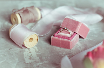romantic present: pink velvet box with a wedding ring and light satin ribbons on a gray background