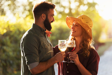 Portrait of young smiling man and woman tasting wine at winery vineyard - Young people enjoying harvest time together. Romantic love.
