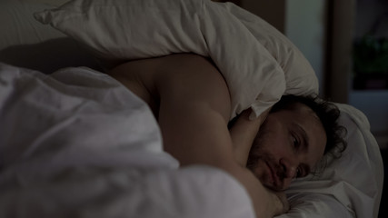 Annoyed man tossing and turning in bed unable to fall asleep, noisy neighbors - obrazy, fototapety, plakaty