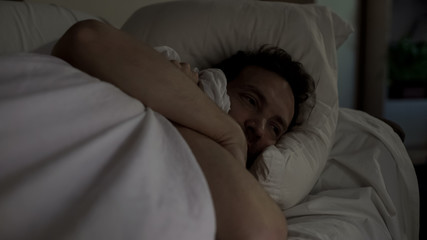Depressed man lying in bed unable to fall asleep, noisy neighbors, insomnia