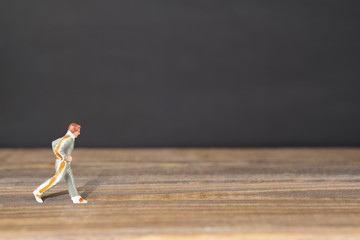 Miniature man running on wooden surface in dark background. Clipping Path of the model included. Copy space. - Powered by Adobe