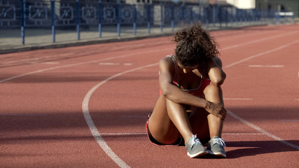 Biracial sportswoman exhausted after tough trainings sitting in middle of track - Powered by Adobe