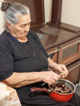 Old Fashioned Elder Woman Holding A Pot With Chestnuts And Peeling Them