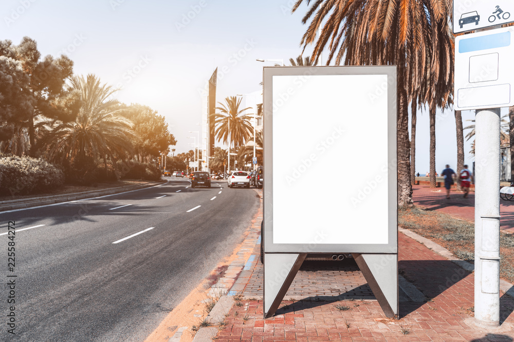 Wall mural Outdoor empty informational board placeholder; white blank city billboard mock-up near the road; vertical blank advertising banner template on the sidewalk between the embankment and the highway