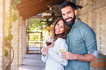 Portrait of young smiling man and woman tasting wine at winery vineyard - Young people enjoying harvest time together. Romantic love.