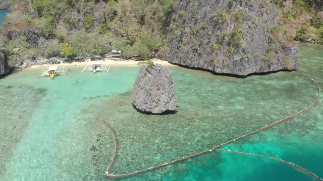 Aerial orbit drone shot around a limestone cliff, in turquoise lagoon, near paraw boats, on a paradise isle, on a sunny day, at Coron island, Philippines, Asia