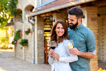 Portrait of young smiling man and woman tasting wine at winery vineyard - Young people enjoying harvest time together. Romantic love.