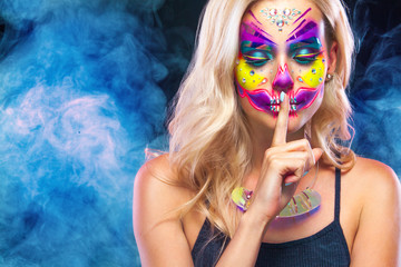 Creative portrait of Sugar Skull on dark background with copyspace. Neon makeup for Halloween or Dia De Mertos holiday.