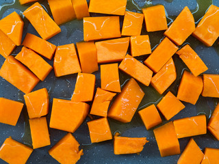 Chopped pumpkin being drizzled with olive oil before baking on a tin