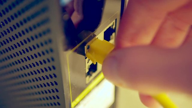 Close up shot of unplugging and plugging in a yellow ethernet cable into a wifi modem and router.