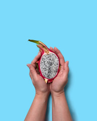 Half of an organic exotic fruit pitahaya hold the woman's hands on a blue background with space for text. Flat lay
