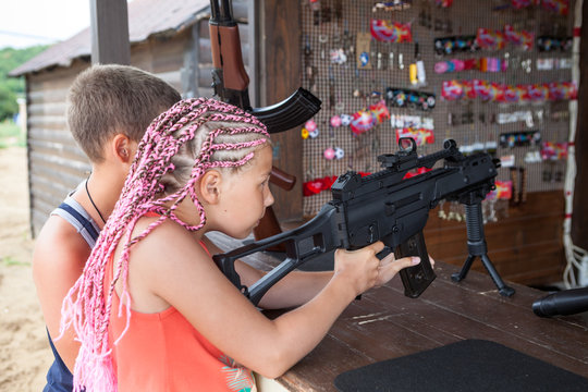 Young girl with dreds shoots with gun in shooting range, brother standing by side
