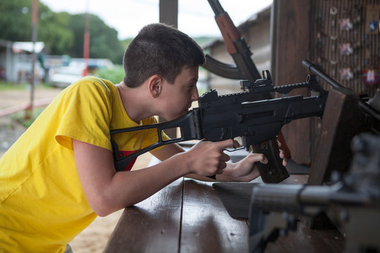 Teenage boy aiming with pneumatic rifle in shooting galery, side view