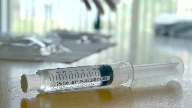 Medical nurse doing an at home patient visit putting on sterile gloves and picking up a syringe of saline solution.