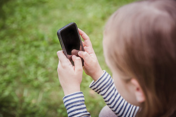 Cute little girl is using the smart phone. grass on background.