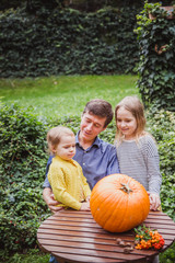 Happy halloween. Father and two daughters look at the face cut in the pumpkin for Halloween outside.