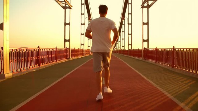 back view of a male runner. guy wearing white t-shirt jogging along the bridge.