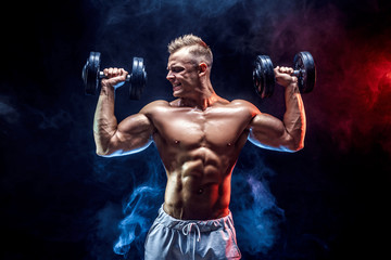 Handsome bodybuilder doing Exercise for the shoulder muscles, deltoid with dumbbell. Studio shot. Smoke.