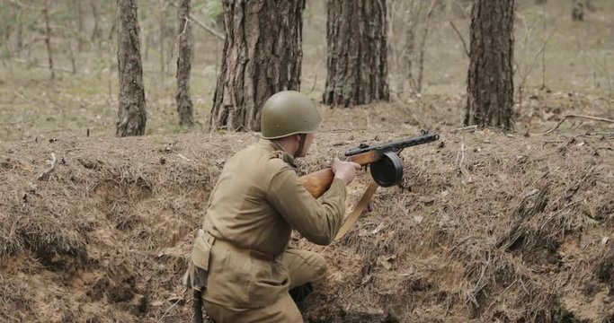 Russian Soviet Infantry Soldier Of World War II Reloading Sub-machine Gun In Forest Trench. Soldier Attacking Enemy In Forest During Historical Reenactment