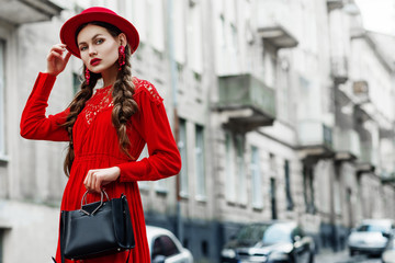 Outdoor portrait of young beautiful fashionable woman wearing total red look: dress, hat, earrings,...