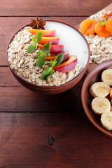 Oatmeal with fruits and green mint. Oat flakes with milk and dried apricots on wooden background. Healthy food for vegans. Dry oats with peaches, anise and berries of mountain ash