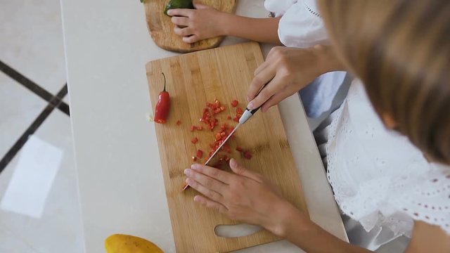 Top view. The two sisters on a wooden board cut pepper chili and avocado for cooking the salad at the kitchen table. Cutting peppers and avocado