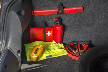 Wnętrze bagażnika samochodu w którym znajduje się apteczka samochodowa, gaśnica, trójkąt ostrzegawczy, kamizelka odblaskowa, kable rozruchowe oraz linka holownicza.