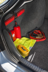 Wnętrze bagażnika samochodu w którym znajduje się apteczka samochodowa, gaśnica, trójkąt ostrzegawczy, kamizelka odblaskowa, kable rozruchowe oraz linka holownicza.