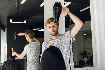 Male hairdresser smiling and talking with a customer while making a new haircut to beutiful young...