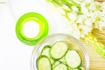 Cucumber home spa and hair care concept. Sliced cucumber, bottles of oil, candle, bathroom towel. Straw light background