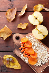Oatmeal with different fruits and honey. Oat flakes with milk and dried apricots on wooden background. Healthy food for vegan. Dry oats with berries of mountain ash and green mint. Autumn pattern