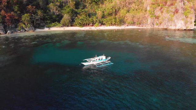 Aerial drone shot around a Paraw boat, in shallow, turquoise sea, around a beautiful, tropical isle, at Coron island, in Philippines, Asia