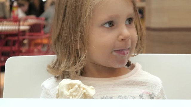 Little Girl Child eats an Ice Cream Cone sitting in a Mall Cafe