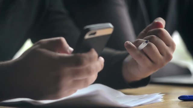 Close-up a Man making Notes with a Pen, Paper and Mobile Smart Phone in Hands