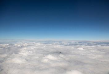 view from window of airplane, clouds below, blue sky, above the clouds